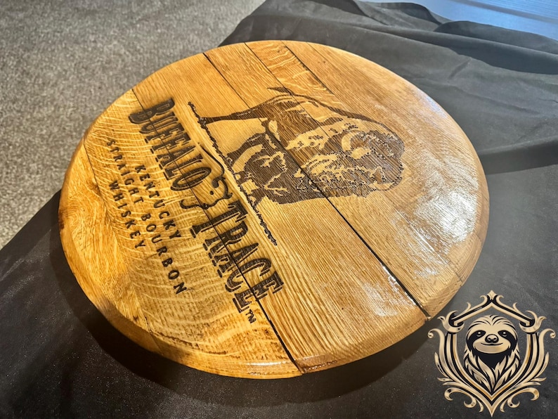 May include: Circular wooden lid from a Buffalo Trace whiskey barrel. The lid is made of light brown wood and features the brand name and a bison illustration. The text reads "Straight Kentucky Bourbon Whiskey."