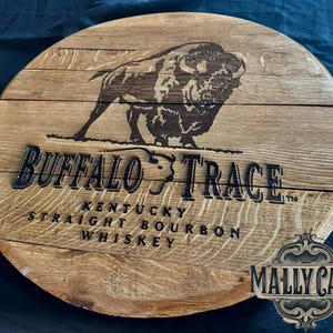 May include: A circular wooden sign featuring the words "Buffalo Trace" and a bison illustration. The sign also includes the text "Kentucky Straight Bourbon Whiskey." The sign is made of light brown wood.