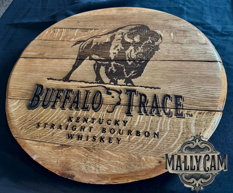 May include: A circular wooden sign featuring the words "Buffalo Trace" and a bison illustration. The sign also includes the text "Kentucky Straight Bourbon Whiskey." The sign is made of light brown wood.