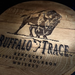 May include: A wooden barrel head featuring the words "Buffalo Trace" and a bison illustration. The text "Kentucky Straight Bourbon Whiskey" is also visible. The wood has a natural grain and a warm, brown tone.