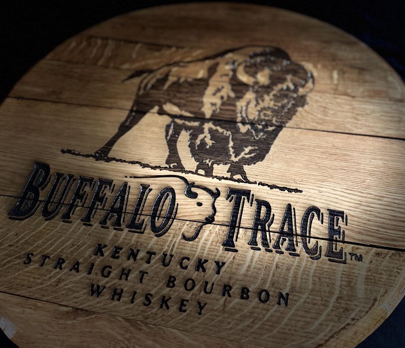 May include: A wooden barrel head featuring the words "Buffalo Trace" and a bison illustration. The text "Kentucky Straight Bourbon Whiskey" is also visible. The wood has a natural grain and a warm, brown tone.