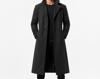 May include: A full-length, dark gray coat with a classic design. The coat features a notched collar, button closure, and front pockets. The model is wearing a black t-shirt, black pants, and black boots. The coat is a stylish outerwear option.