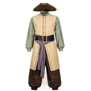 Pode incluir: Um conjunto de fantasia composto por um chapéu tricórnio castanho, uma camisa de manga comprida verde sálvia, um colete bege sem mangas com botões dourados, um cinto preto com fivela dourada, uma faixa roxa e calças castanho-escuras.