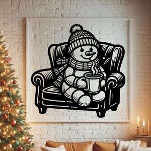 Op de afbeelding: Een zwart-wit wanddecoratie met een sneeuwpop met een gebreide muts en sjaal, zittend in een fauteuil terwijl deze een dampende mok vasthoudt. Het grafische ontwerp wordt getoond in een vierkante lijst aan een witte bakstenen muur.