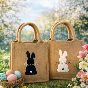 Könnte beinhalten: Zwei Jutetaschen mit Hasenmotiven und Namen. Eine Tasche hat einen schwarzen Hasen mit dem Namen "Paul", die andere einen weißen Hasen mit dem Namen "Felix". Beide Hasen haben ein Herz. Ostermotiv.