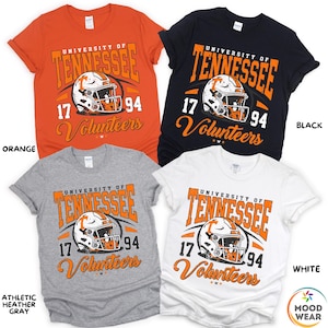 May include: Four short-sleeved t-shirts in orange, black, athletic heather gray, and white. Each shirt features the text "University of Tennessee" and "Volunteers" with a football helmet graphic. The numbers "17" and "94" are also displayed.