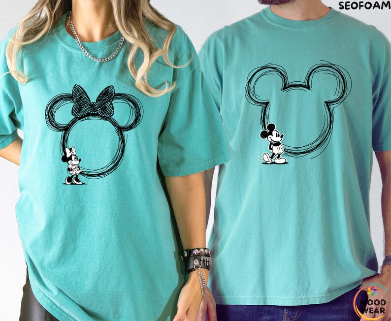 May include: Two turquoise t-shirts with black Mickey Mouse and Minnie Mouse designs. The Minnie Mouse shirt features a bow and a Minnie Mouse figure. The Mickey Mouse shirt has a Mickey Mouse figure. Both designs are inside a circular outline.