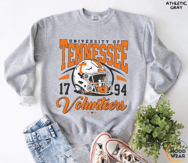 May include: Athletic gray sweatshirt with the text "University of Tennessee" in orange, along with a football helmet graphic. The sweatshirt also features the numbers "17" and "94" and the word "Volunteers".