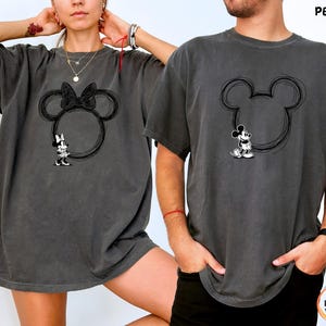 May include: Two dark gray t-shirts featuring a Mickey Mouse design. One shirt has a Minnie Mouse design with a bow, and the other has a Mickey Mouse design. The word "PEPPER" is printed on the top right of the image.
