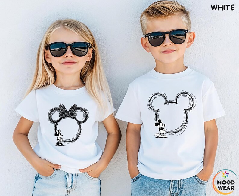 May include: Two children wearing white t-shirts with black Mickey Mouse and Minnie Mouse designs. The Mickey Mouse design is on the right, and the Minnie Mouse design is on the left. Both children are wearing black sunglasses and blue jeans.