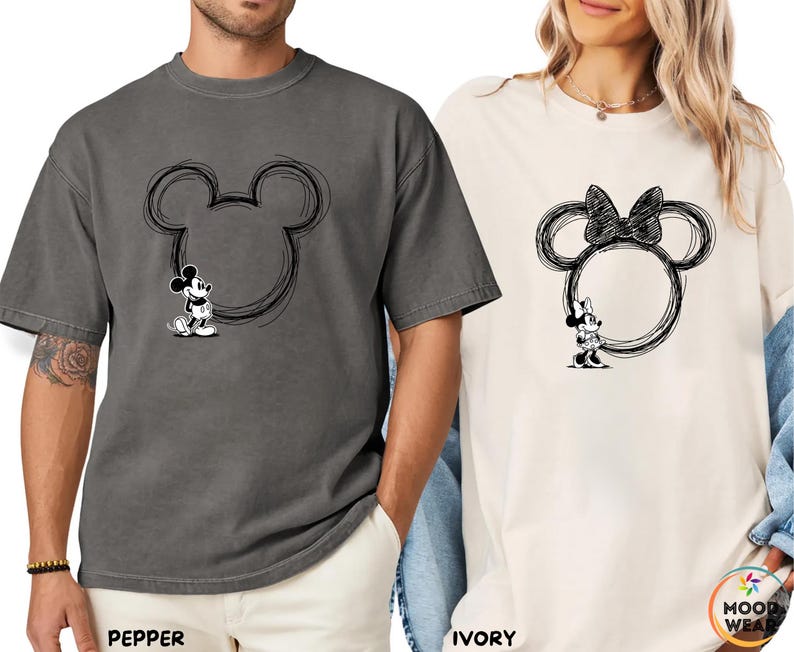May include: Two t-shirts, one pepper-colored and one ivory-colored, each featuring a black sketch of Mickey and Minnie Mouse. The Mickey Mouse shirt has a black outline of his head with Mickey standing inside. The Minnie Mouse shirt has a bow on top.