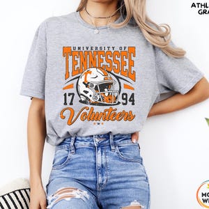May include: Athletic gray t-shirt featuring the University of Tennessee Volunteers logo. The design includes the text "University of Tennessee," a football helmet graphic, and the numbers "17" and "94." The word "Volunteers" is written in a script font.