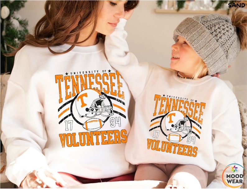 May include: Two white crewneck sweatshirts featuring a distressed orange and black graphic that reads University of Tennessee Volunteers, with a football helmet displaying a T logo and a football, plus the numbers 17 and 94 on the sides.
