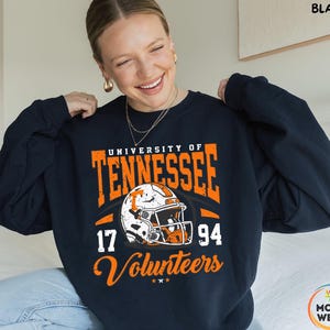 May include: A navy blue sweatshirt with orange and white graphics. The design features the words "University of Tennessee" and "Volunteers" along with a football helmet and the numbers "17" and "94". The sweatshirt is a crew neck style.
