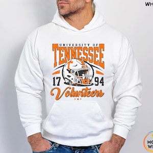 May include: White hoodie featuring the University of Tennessee Volunteers logo in orange and white. The design includes a football helmet, the years 17 and 94, and the word "Volunteers". The hoodie has a front pocket and a drawstring hood.