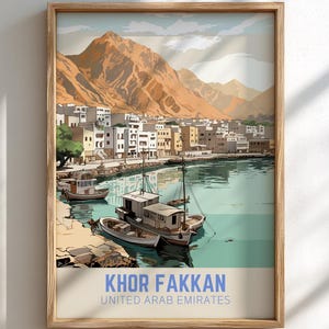 Puede incluir: Una impresión artística enmarcada de Khor Fakkan, Emiratos Árabes Unidos. La obra de arte representa una ciudad costera con barcos en el agua, edificios y montañas al fondo. La paleta de colores incluye tonos de azul, beige y marrón.