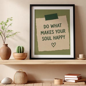 Pu&ograve; includere: Una stampa artistica con cornice nera che presenta una nota di carta color marrone chiaro fissata con nastro adesivo verde scuro su uno sfondo verde oliva. Il testo recita DO WHAT MAKES YOUR SOUL HAPPY sopra un piccolo cuore disegnato a mano.