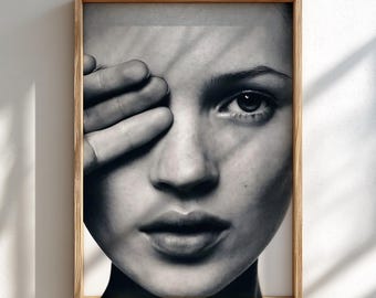 May include: A black and white framed portrait print featuring a close-up of a face with one hand partially covering the eye. The image displays high-contrast lighting with distinct shadows cast across the skin, housed in a light-toned wooden frame.