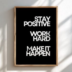 May include: A rectangular wall art print in a light wood frame featuring a black background with white text that reads STAY POSITIVE, WORK HARD, MAKE IT HAPPEN. The typography is clean, bold, and sans-serif, centered within the frame.