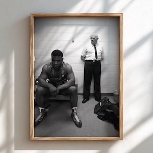 Könnte beinhalten: Ein schwarz-weiß gerahmtes Foto, das einen muskulösen Boxer zeigt, der auf einer Bank sitzt und ein Unterhemd sowie Boxstiefel trägt, während ein Mann mit kurzärmeligem Hemd und Krawatte hinter ihm vor einer gefliesten Wand steht.