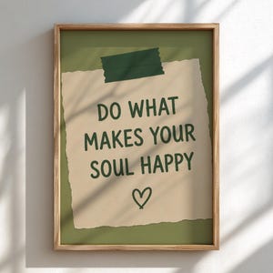 Pu&ograve; includere: Una stampa da parete incorniciata con un foglietto di carta beige dai bordi strappati su uno sfondo verde oliva. Il foglietto riporta il testo verde scuro DO WHAT MAKES YOUR SOUL HAPPY e un piccolo cuore disegnato a mano, fissato con un nastro adesivo verde scuro.
