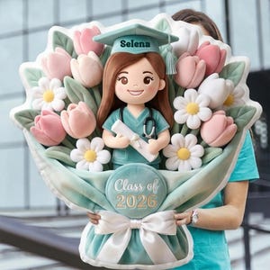 Puede incluir: Un ramo de graduación de peluche con una muñeca de enfermera sonriente que lleva una gorra con el nombre "Selena". El ramo incluye tulipanes rosas, margaritas blancas y el texto "Class of 2026". El ramo está atado con una cinta blanca.