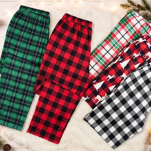 Peut inclure: Cinq paires de pantalons de pyjama avec divers motifs, notamment un tartan vert et noir, un motif à carreaux rouge et noir, un tartan rouge et blanc, un fond rouge avec des rennes et des sapins blancs, et un motif à carreaux noir et blanc.