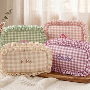 Könnte beinhalten: Vier rechteckige Kosmetiktaschen mit Vichy-Karo in Pastellfarben: Grün, Rosa, Beige und Lila. Jede Tasche hat einen gerüschten Rand und einen gestickten Namen: Avery, Ella, Riley und Rachel. Die Taschen werden auf einem Holztablett präsentiert.