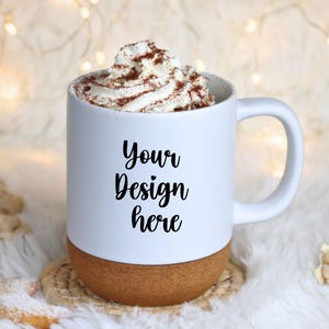 Puede incluir: Taza blanca con base de corcho, llena de crema batida y cacao en polvo. La taza tiene el texto "Your Design here" en escritura negra. La taza está sobre un posavasos tejido.