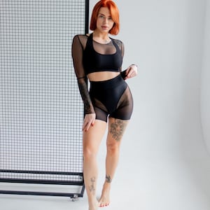 Puede incluir: Conjunto deportivo negro con top corto de cuello halter, top de malla de manga larga y shorts de cintura alta con paneles de malla. El conjunto est&aacute; dise&ntilde;ado para fitness o baile, ofreciendo un look elegante.