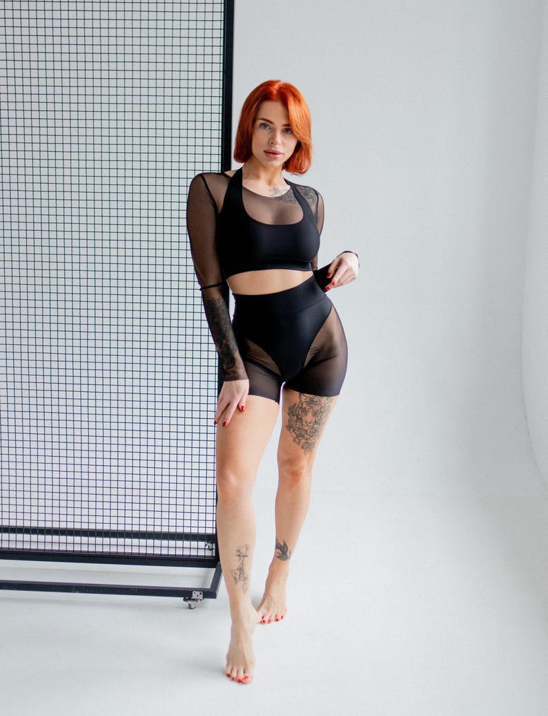 Puede incluir: Conjunto deportivo negro con top corto de cuello halter, top de malla de manga larga y shorts de cintura alta con paneles de malla. El conjunto est&aacute; dise&ntilde;ado para fitness o baile, ofreciendo un look elegante.