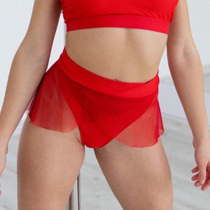 May include: A red two-piece dance outfit. The top is a sports bra style. The bottom is a pair of shorts with a sheer, flowing skirt overlay. The outfit is made of a solid red material.