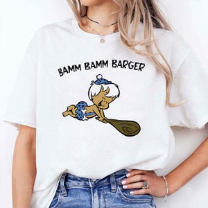 May include: White t-shirt with a cartoon illustration of Bamm-Bamm Rubble from The Flintstones. The character is shown in a blue and white outfit, holding a wooden club. The text "BAMM BAMM BARGER" is printed above the character.