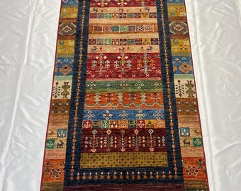 Könnte beinhalten: Ein rechteckiger, mehrfarbiger Teppich mit einem zentralen Design aus roten, blauen, orangefarbenen und grünen Streifen. Der Teppich weist komplizierte Muster und einen Fransenrand auf. Der Teppich ist etwa 91 cm breit und 244 cm lang.