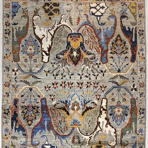 May include: A rectangular area rug featuring a light grey background with a complex, symmetrical pattern of stylised floral and organic motifs in shades of blue, rust orange, cream, and dark brown, finished with a short white fringe at both ends.