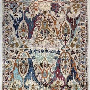 May include: A rectangular area rug featuring a complex, symmetrical pattern with intricate floral and botanical motifs in shades of deep blue, rust orange, light blue, and cream. The design includes a decorative border and fringed edges.