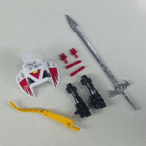 May include: A collection of toy robot parts, including a silver sword, two black blasters, a white and red shield, two red connectors, two red missile tips, and a yellow bow-shaped piece. The parts are arranged on a white surface.
