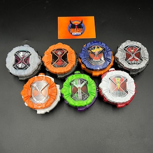 May include: Seven toy watches in various colours, including orange, blue, green, and red. Each watch has a detailed face and a circular shape. The image also shows a logo with the text "MAHU SUNTOY".