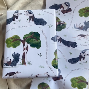 May include: White wrapping paper featuring a repeating pattern of anteaters, trees, and logs. The anteaters are illustrated in brown, black, and white, with a playful design. The trees are green with brown trunks.