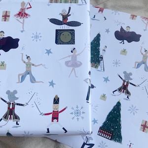 May include: Two rolls of white wrapping paper with a festive ballet theme. The paper features illustrations of ballerinas, nutcrackers, mice, snowflakes, Christmas trees, and gift boxes in red, blue, and gold.