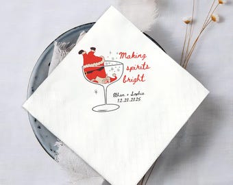 May include: White square napkin with a cartoon Santa Claus in a cocktail glass. The napkin has the text "Making spirits bright" in red script, along with a date and names. Festive holiday party supplies.
