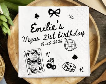 Op de afbeelding: Witte vierkante papieren servet met zwarte illustraties en tekst. De tekst luidt "Emilie's Vegas 21st birthday 01.25.2026". Het servet heeft een strik, speelkaart, kersen, dobbelstenen, discobal en andere symbolen.