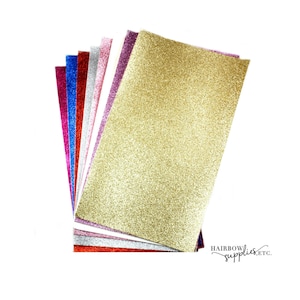 K&ouml;nnte beinhalten: Ein Stapel aus 10 Bl&auml;ttern Glitzerpapier in verschiedenen Farben, darunter Gold, Silber, Rot, Pink, Blau und Wei&szlig;. Das Papier ist mit Glitzer texturiert und perfekt f&uuml;r Bastelprojekte.