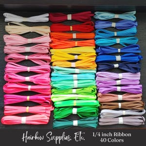 May include: A collection of 40 colors of 1/4 inch ribbon, arranged in rows. The ribbons are tied with white bands and displayed in a variety of colors, including pink, red, orange, yellow, green, blue, and brown. Text at the bottom reads "Hairbow Supplies, Etc."