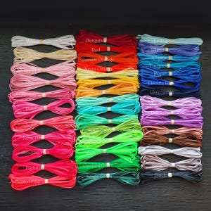 May include: A collection of colorful flat cords, neatly bundled and labeled with color names. Colors include white, ivory, pinks, oranges, greens, blues, and browns. The cords are likely used for crafting or jewelry making.