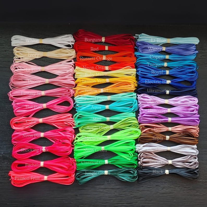 May include: A collection of colorful flat cords, neatly bundled and labeled with color names. Colors include white, ivory, pinks, oranges, greens, blues, and browns. The cords are likely used for crafting or jewelry making.