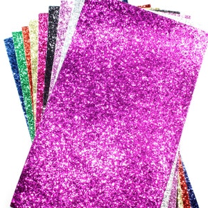 Puede incluir: Una pila de papel de purpurina en varios colores, incluyendo rosa, azul, verde, rojo, dorado y plateado. El papel est&aacute; dispuesto en forma de abanico, con el papel de purpurina rosa en la parte superior.