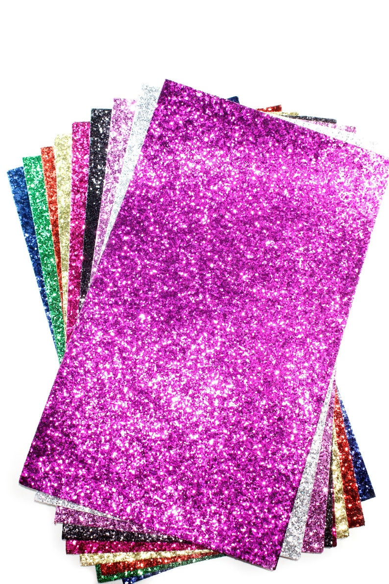 Puede incluir: Una pila de papel de purpurina en varios colores, incluyendo rosa, azul, verde, rojo, dorado y plateado. El papel est&aacute; dispuesto en forma de abanico, con el papel de purpurina rosa en la parte superior.