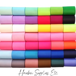 May include: A stack of 24 rolls of satin ribbon in various colors, including pink, blue, green, yellow, and orange. The ribbon is arranged in rows, with each row containing a different color. The ribbon is all the same width and is approximately 1 inch wide. The ribbon is perfect for crafting, decorating, and gift wrapping.