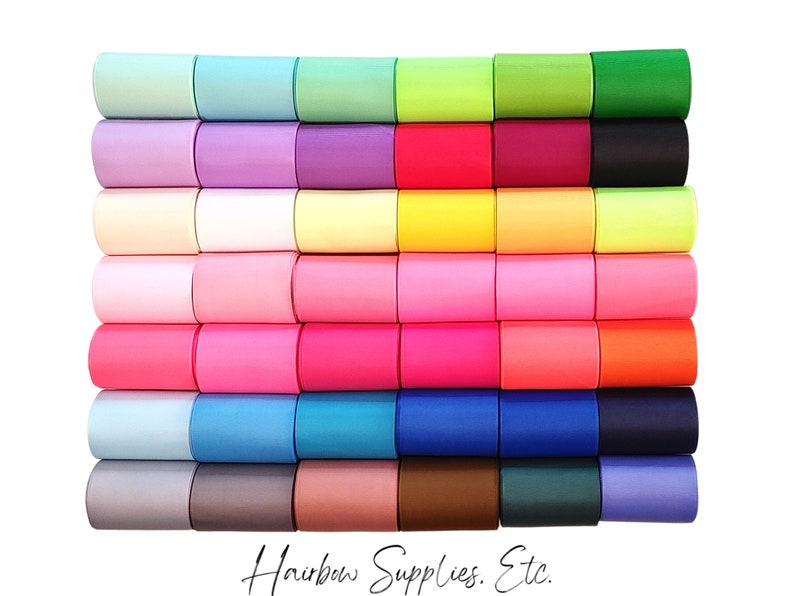 May include: A stack of 24 rolls of satin ribbon in various colors, including pink, blue, green, yellow, and orange. The ribbon is arranged in rows, with each row containing a different color. The ribbon is all the same width and is approximately 1 inch wide. The ribbon is perfect for crafting, decorating, and gift wrapping.